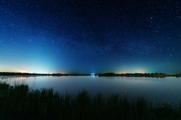 Magic starry night with the galaxy Milky way near the river with a large tree.