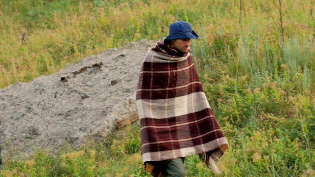 Lonely cowboy with blue hat and poncho walks at field summer time