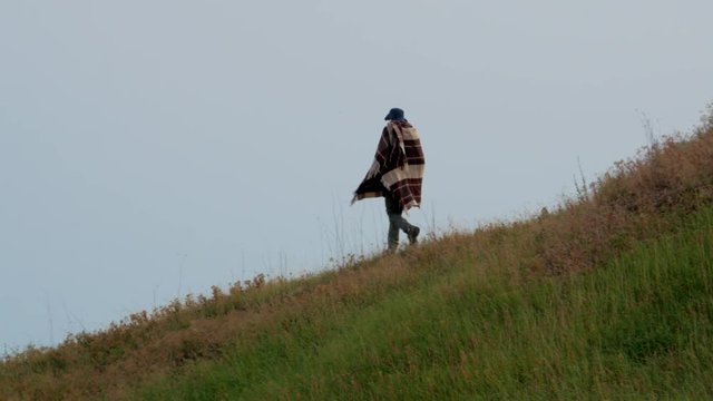 Cowboy with poncho and hat walks down from the hill