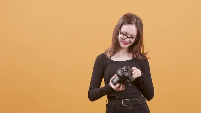 Teenage female photographer takes a picture with her professional camera. Young beautiful artistic grils on yellow background.