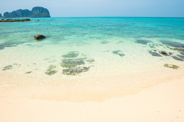 Tropical sea landscape with rocks at sand beach and rocky island at horizon