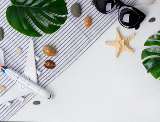 Time to travel concept. Plane, sunglasses, monstera leavs, plane, star fish and towel on white wooden table.