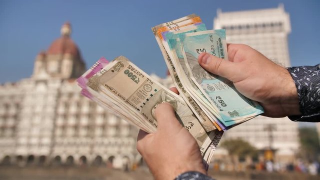 A man considers Indian rupees on the street of Mumbai. Hands close up.