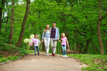 Fototapeta premium Family father and mother with two kids walking in summer green city park on picnic, happy holidays parents and children on nature