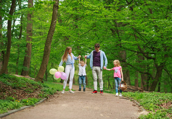 Fototapeta premium Family father and mother with two kids walking in summer green city park on picnic, happy holidays parents and children on nature