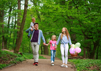 Obraz premium Family father and mother with two kids walking in summer green city park on picnic, happy holidays parents and children on nature