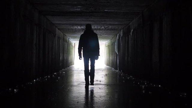 Man silhouette walking in a dark tunnel. Underground, post apocaloptic view. Exit concept. 