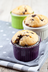 Three homemade fresh muffins on colorful ceramic bowls on linen napkins on rustic wooden table.