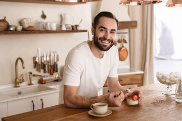 Portrait of caucasian brunette man 20s eating panna cotta dessert while having breakfast at home
