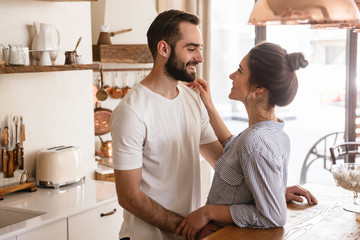 Image of optimistic brunette couple in love smiling while hugging together in apartment