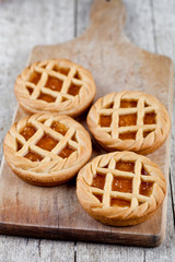 Fresh baked tarts with marmalade or apricot jam filling on cutting board on on rustic wooden table.