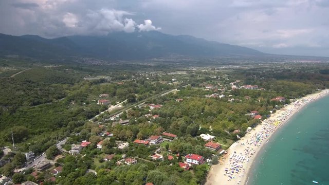 Aerial view of idyllic organized beach in Neo Panteleimona, Katerini, Greece,Beach with umbrellas and trees, at the foot of Mount Olympus, top-down movement by drone