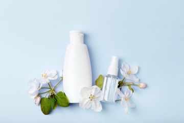 Face care products (tonic or lotion, spray) on blue background with spring apple blossom. Freshness natural anti-age care. Female everyday fresh cosmetics