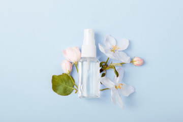 Face care products (tonic or lotion, spray) on blue background with spring apple blossom. Freshness natural anti-age care. Female everyday fresh cosmetics