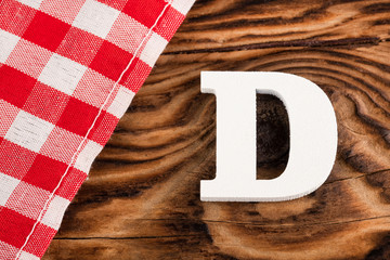 Letter D of the alphabet - Red checkered cloth tablecloth on rustic wood background. Text space