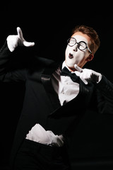 portrait of smiling mime man in tuxedo and glasses on black background