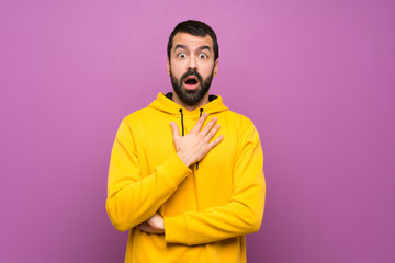 Handsome man with yellow sweatshirt surprised and shocked while looking right