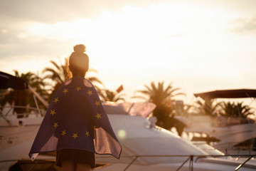 Child teenager girl at background of the sea and yachts an European Union flag on her shoulders. Sunset time