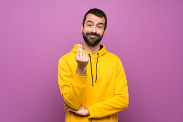 Handsome man with yellow sweatshirt making money gesture