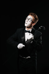 portrait of mime man in tuxedo and glasses posing with walking stick on black background