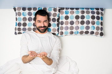 Man in bed in top view holding copyspace imaginary on the palm to insert an ad