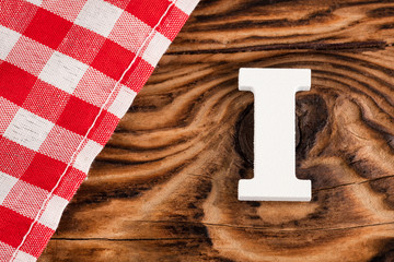 Letter I of the alphabet - Red checkered cloth tablecloth on rustic wood background. Text space