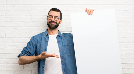 Handsome man with beard over white brick wall holding an empty placard