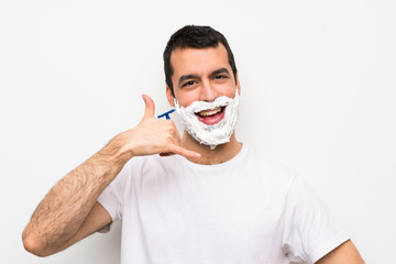 Man shaving his beard over isolated white background making phone gesture. Call me back sign