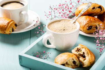 Holiday break with cup of coffee, mini fresh croissants chocolate bun and carnation flowers on turquoise background.