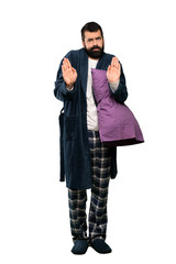 Man with beard in pajamas making stop gesture and disappointed over isolated white background