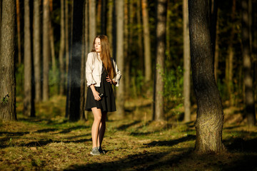 Vape teenager. Young cute girl in casual clothes smokes an electronic cigarette outdoors in the forest at sunset in summer. Bad habit that is harmful to health. Vaping activity.