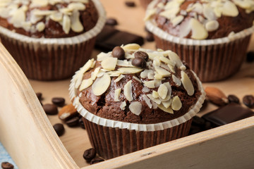 Delicious, sweet chocolate muffins, with almond petals in a wooden tray next to grains of coffee on a blue wooden table.