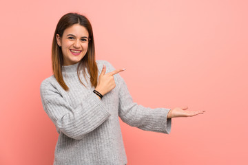 Young woman over pink wall holding copyspace imaginary on the palm to insert an ad