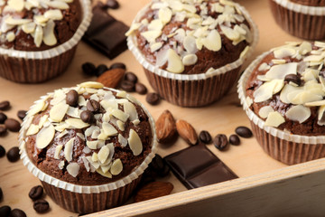Delicious, sweet chocolate muffins, with almond petals in a wooden tray next to grains of coffee on a blue wooden table.