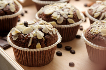Delicious, sweet chocolate muffins, with almond petals in a wooden tray next to grains of coffee on a blue wooden table.