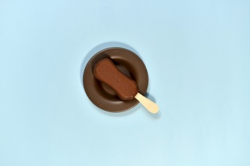 Chocolate ice cream on a stick. In a saucer, on a blue background, in the center. View from above.