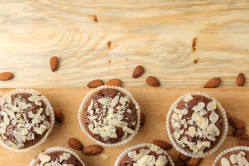 Delicious, sweet chocolate muffins, with almond petals next to almond nuts on a natural wooden table. top view