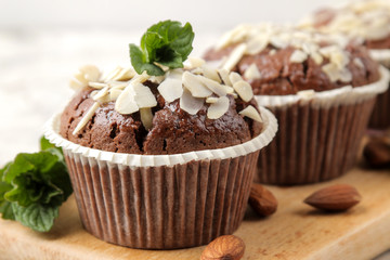 Delicious, sweet chocolate muffins, with almond petals next to mint and almond nuts on a light concrete table. close-up