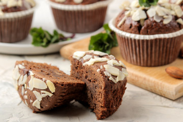 Delicious, sweet chocolate muffins, with almond petals next to mint and almond nuts on a light concrete table. close-up