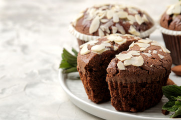 Delicious, sweet chocolate muffins, with almond petals next to mint and almond nuts on a light concrete table. close-up