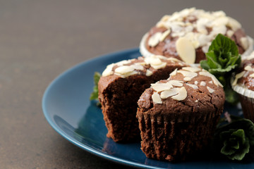 Delicious, sweet chocolate muffins, with almond petals next to mint and almond in a plate on a dark table.