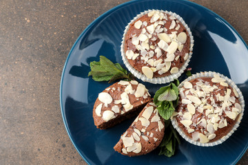 Obraz na płótnie Canvas Delicious, sweet chocolate muffins, with almond petals next to mint and almond in a plate on a dark table. top view