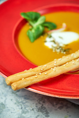 Red plate with pumpkin soup. Light gray textured background. Beautiful serving of dishes. Restaurant menu