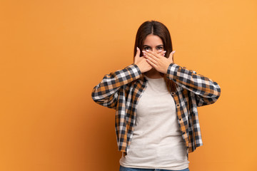Young woman over brown wall covering mouth with hands