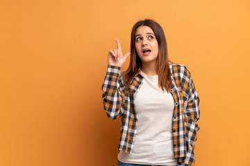 Young woman over brown wall intending to realizes the solution while lifting a finger up