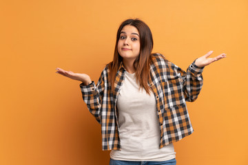 Young woman over brown wall making doubts gesture