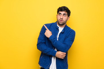 Fototapeta premium Man with blue jacket over yellow wall surprised and pointing side