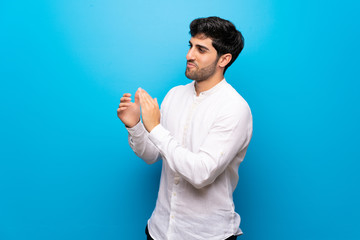 Young man over isolated blue wall applauding after presentation in a conference