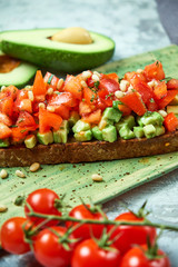 On a green plate of brusket with tomatoes and avocado. Light gray textured background. Beautiful serving of dishes. Restaurant menu