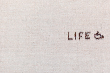 Life word with a cup made from coffee beans on linen texture, arranged middle right.